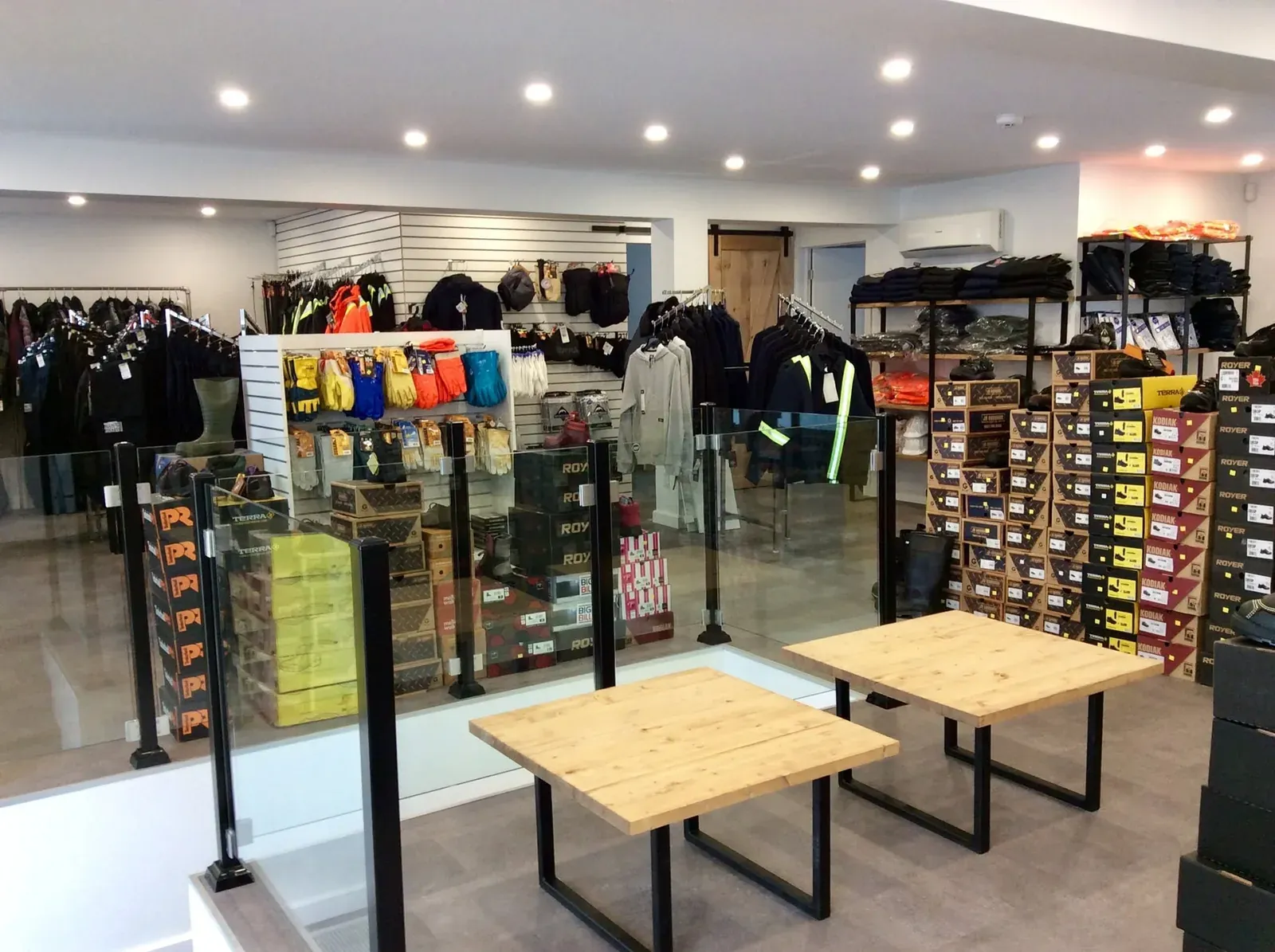 Intérieur du Magasin du Travailleur : allée centrale, présentoirs de vêtements et tablettes de boîtes de bottes jusqu'au plafond.