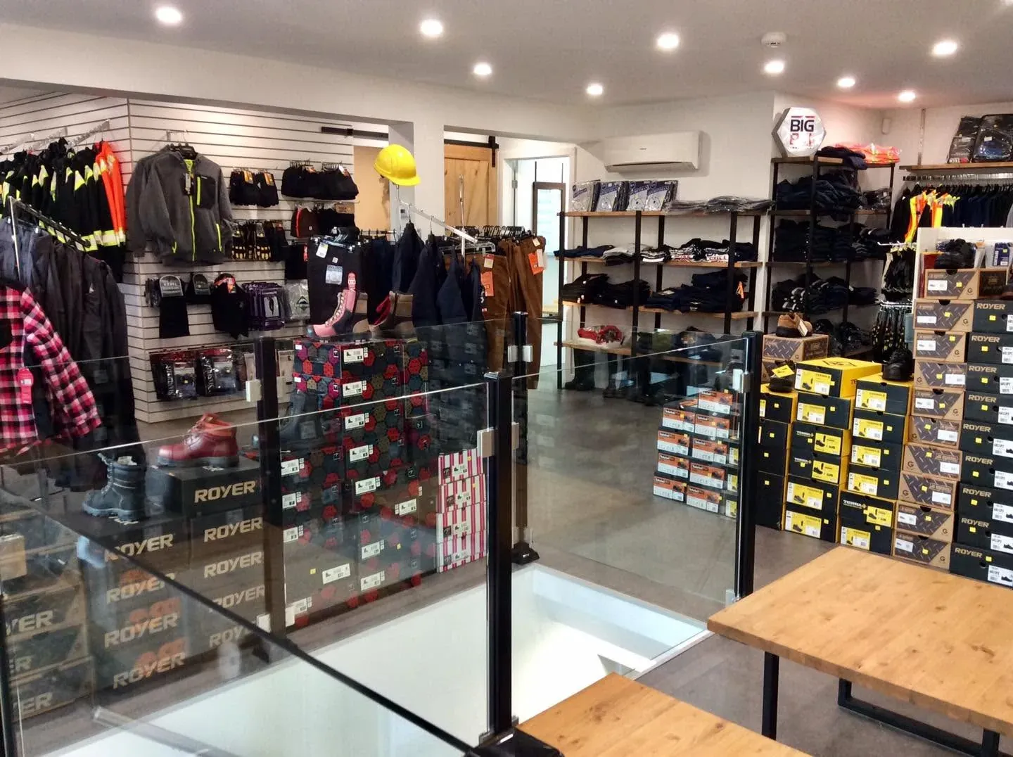 Vue du magasin depuis l'entrée : penderies de manteaux et de chemises, rangées de boîtes de bottes au fond.