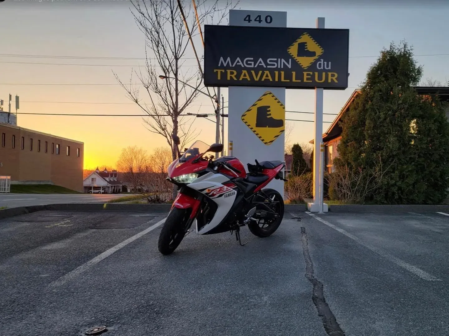 L'enseigne du Magasin du Travailleur au 440, éclairée par un ciel de fin de journée, avec une moto stationnée devant.